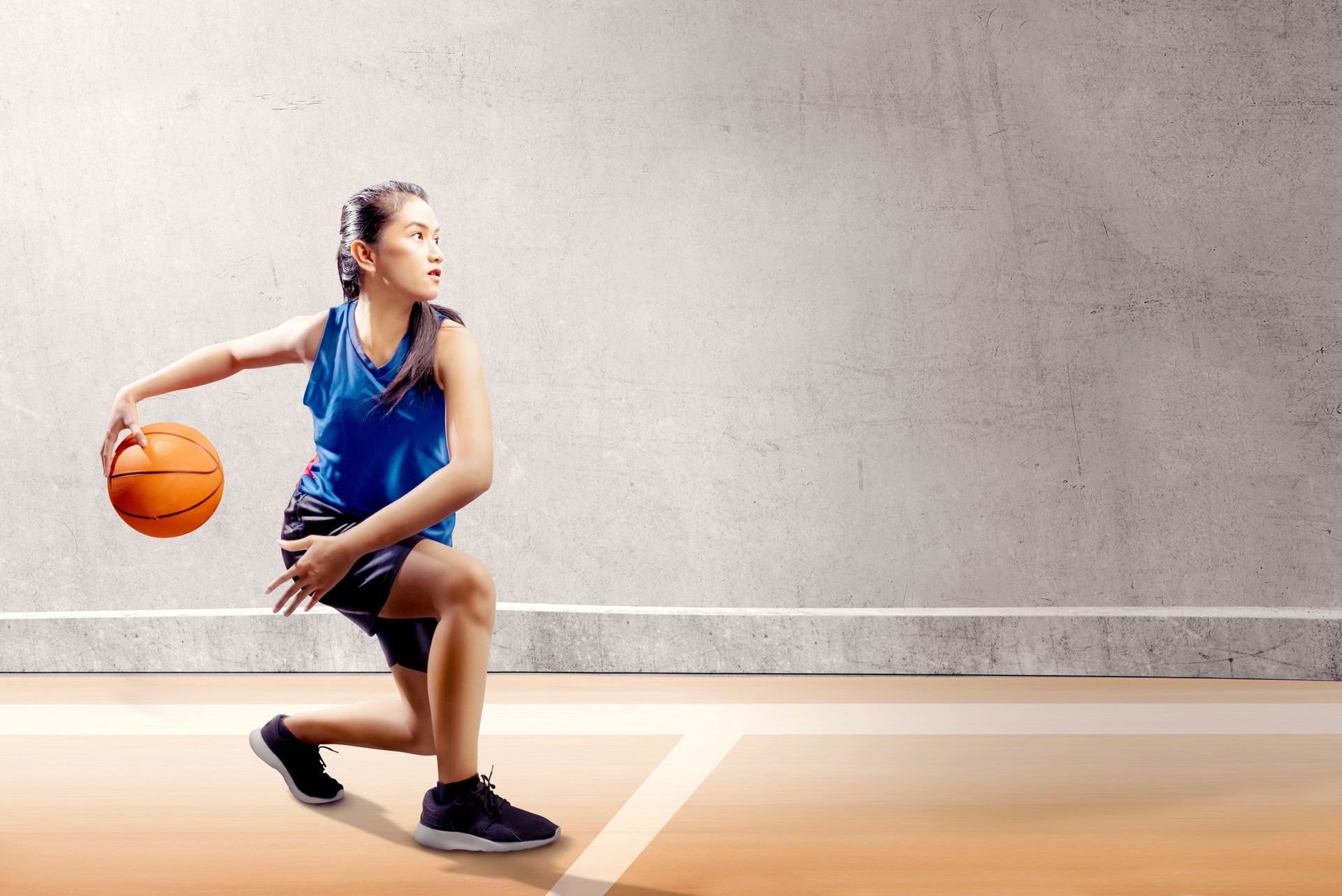 Attractive asian girl in blue sport uniform on basketball pivot moves on the basketball court